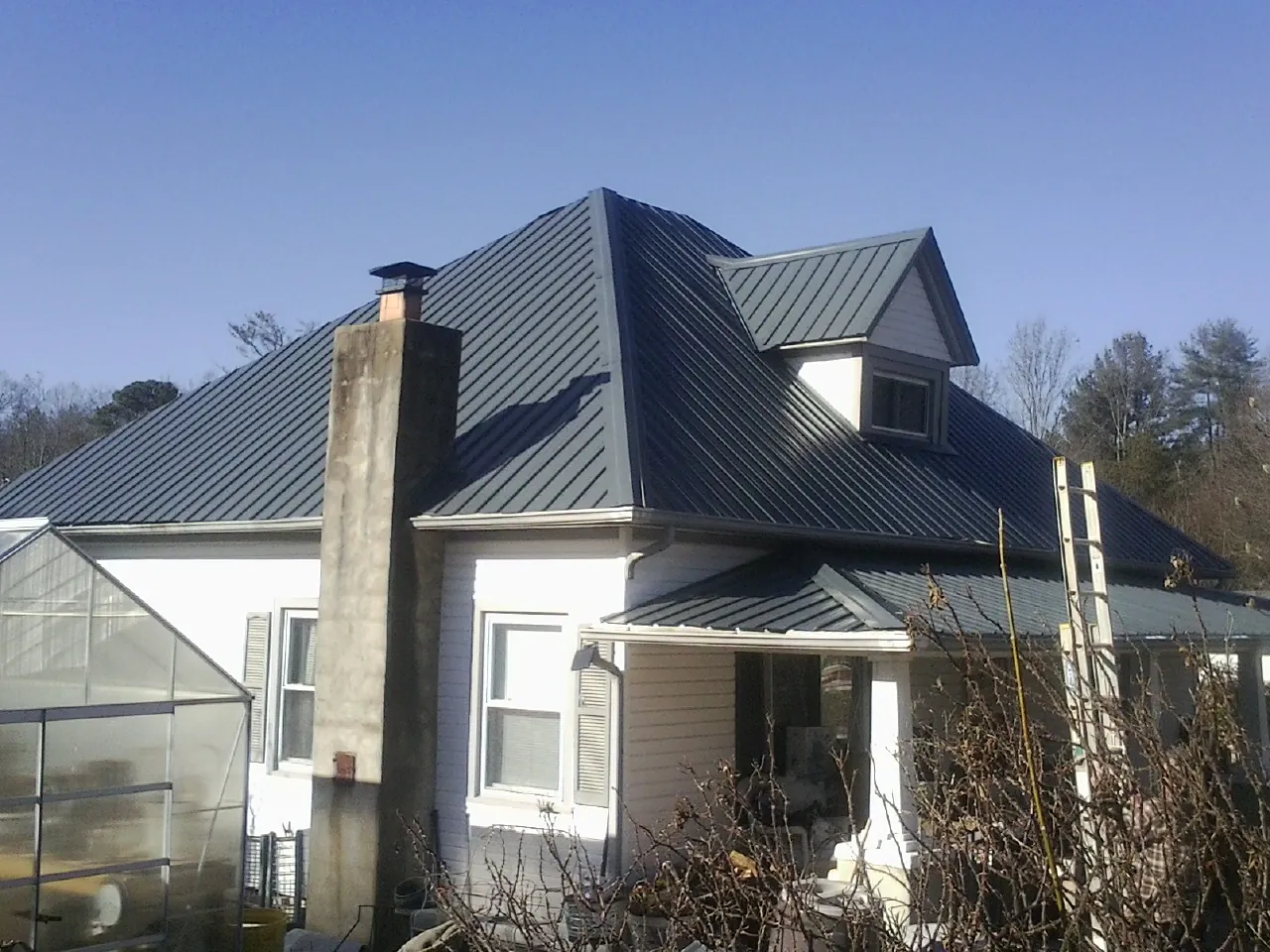Dark blue standing seam metal roof on a white farmhouse with dormer — Slate & Tile Roof Repair by Roofing Brothers in Marcus