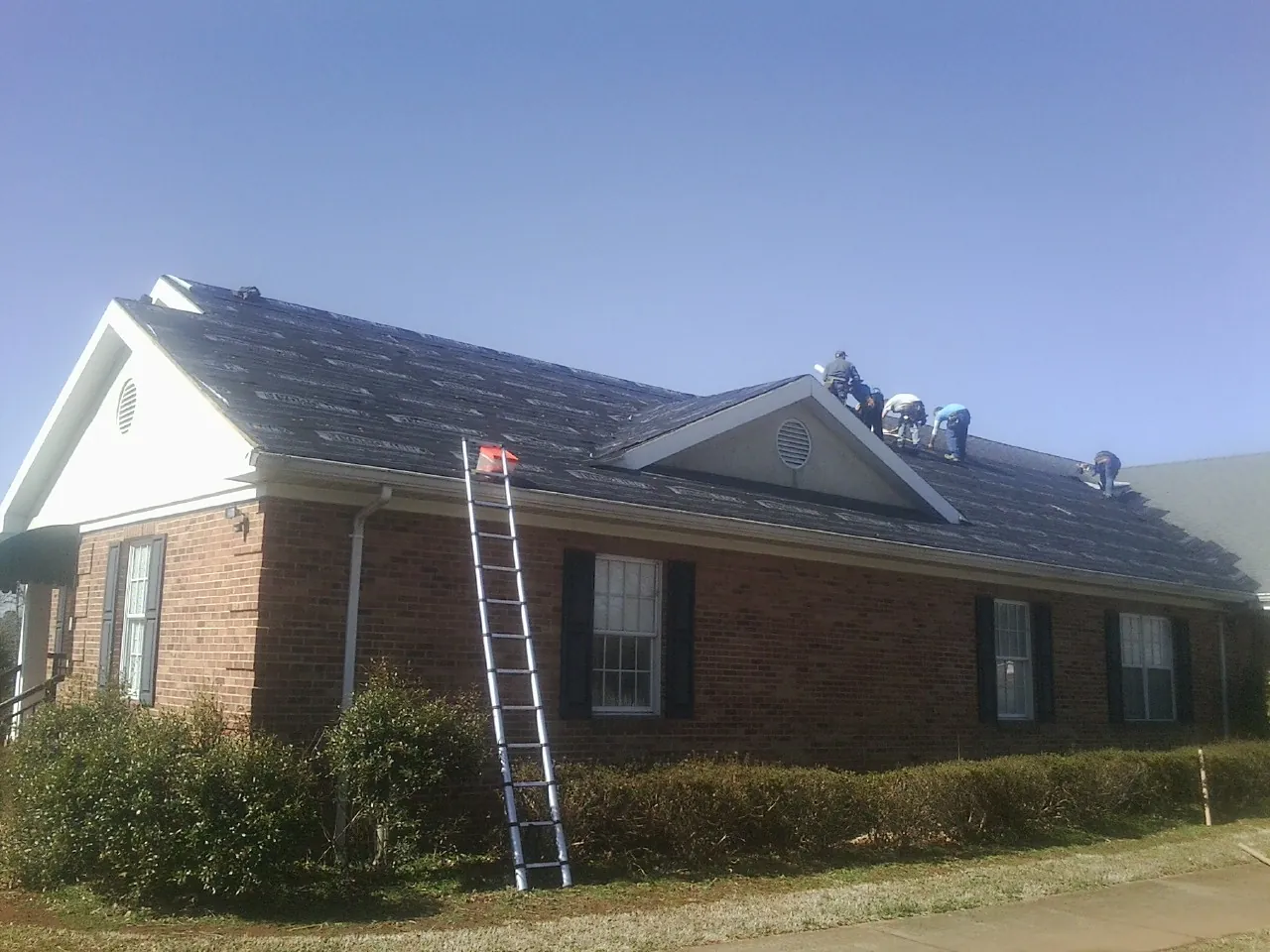 Crew tearing shingles off a brick ranch roof with a ladder set — Metal Roof Repair work by our crew in Marcus