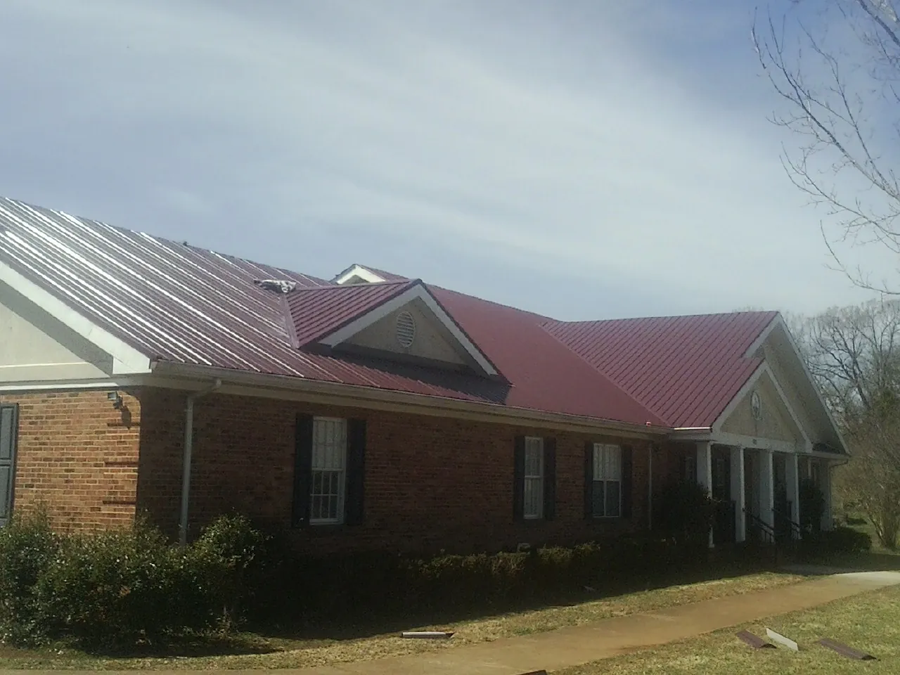 Red metal roof with gabled entries on a long brick building, from a Hail Damage Roof Repair job in Marcus