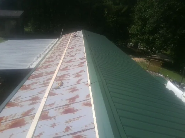Old rusted panels beside newly installed green metal roofing — Wind Damage Roof Repair by Roofing Brothers in Marcus