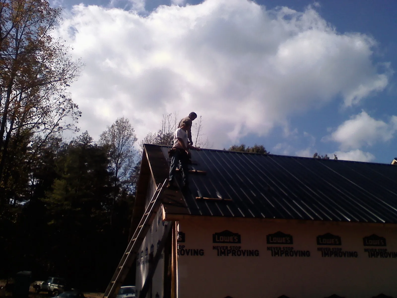 Roofer fastening dark metal panels high against a cloudy sky, from a Roof Inspection job in Marcus