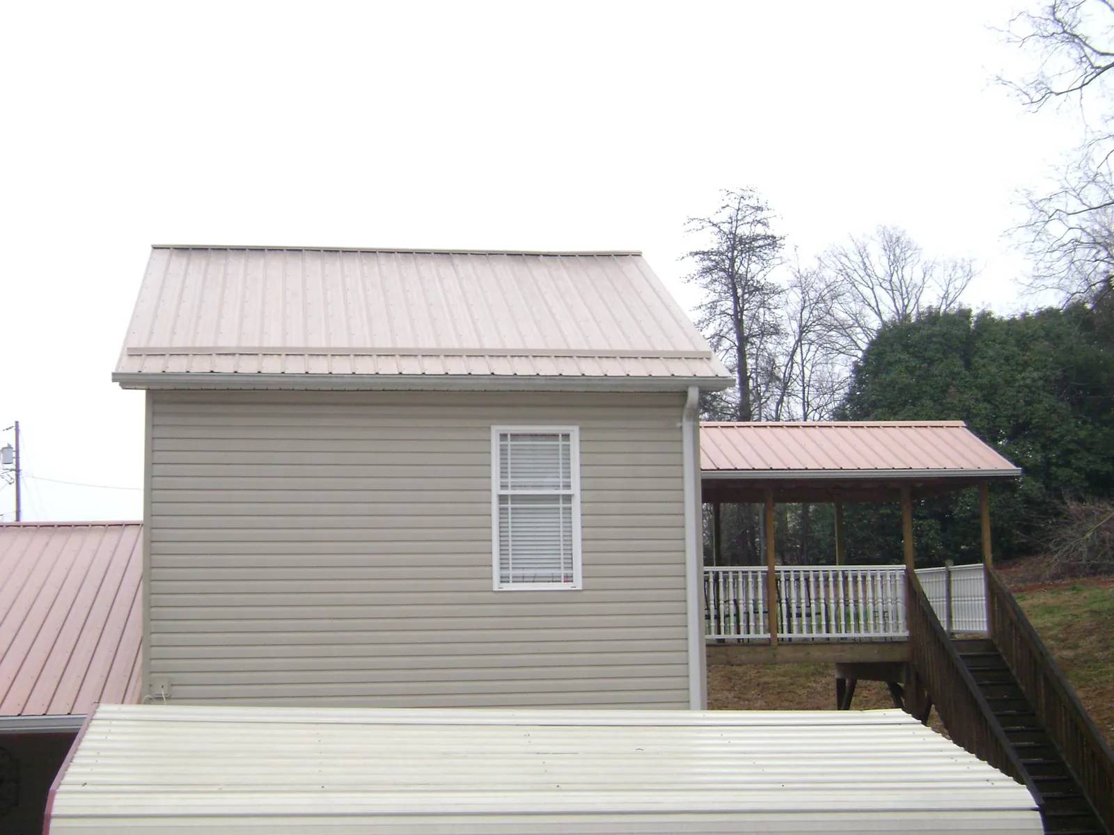 Tan metal roofs on a two story addition and attached porch, from a Roof Replacement job in Marcus